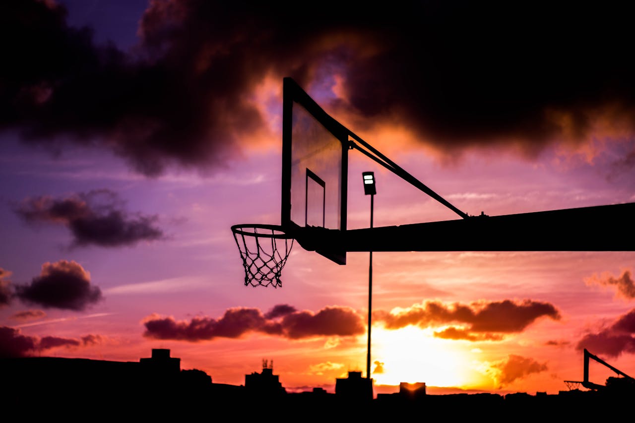 about-img Stunning silhouette of a basketball hoop against a vivid sunset sky with dramatic clouds.